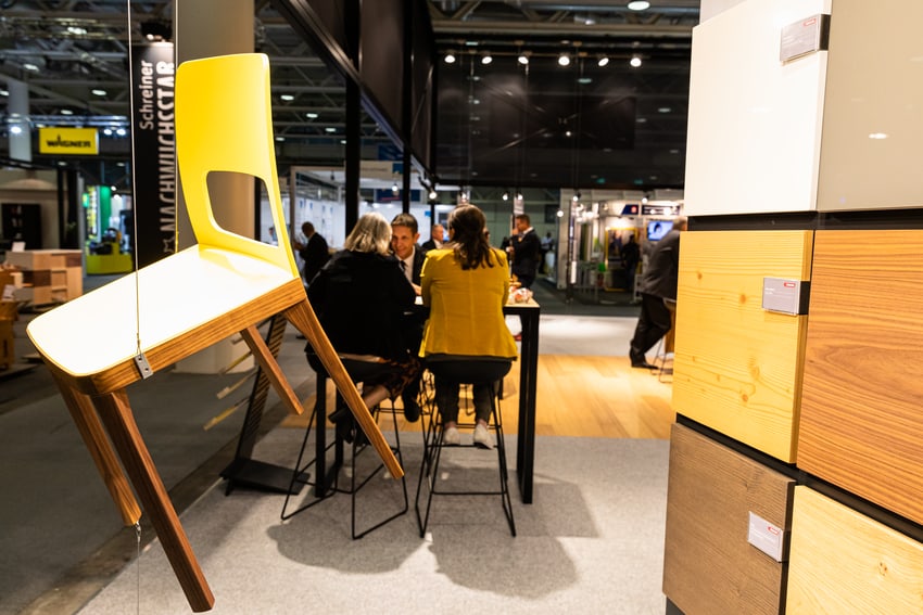 Chaise flottante en panneaux de bois avec les visiteurs du stand en arrière-plan.